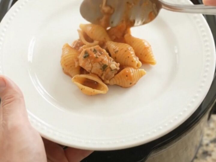 Slow cooker chicken and pasta shells in creamy red pepper sauce topped with melted provolone