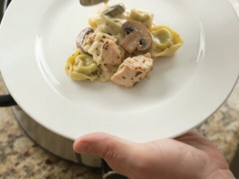Creamy Crockpot chicken spinach tortellini Alfredo with melted mozzarella and cream cheese, served in a black slow cooker.