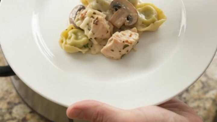 Creamy Crockpot chicken spinach tortellini Alfredo with melted mozzarella and cream cheese, served in a black slow cooker.