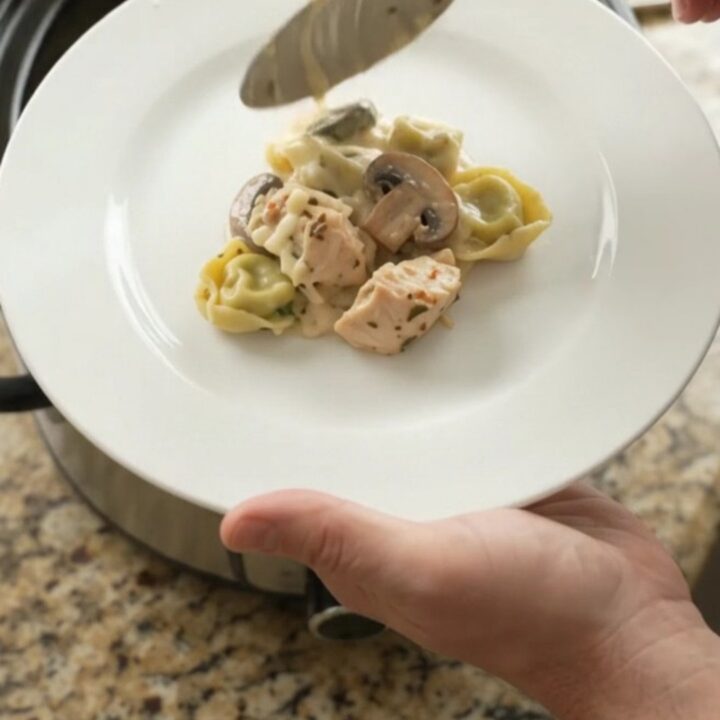 Creamy Crockpot chicken spinach tortellini Alfredo with melted mozzarella and cream cheese, served in a black slow cooker.