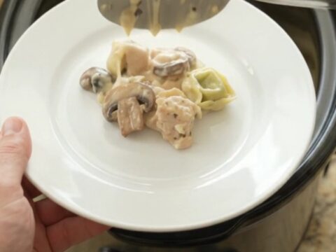 Crockpot chicken spinach tortellini Alfredo with melted provolone and ricotta, served in a slow cooker.