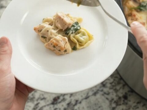 Creamy crockpot chicken spinach tortellini in a black slow cooker, topped with melted Italian cheeses