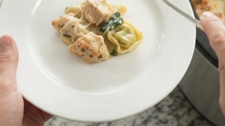 Creamy crockpot chicken spinach tortellini in a black slow cooker, topped with melted Italian cheeses