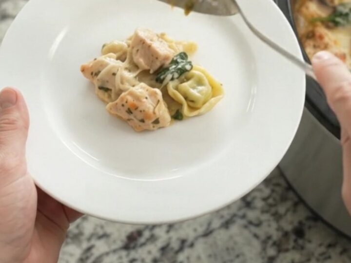 Creamy crockpot chicken spinach tortellini in a black slow cooker, topped with melted Italian cheeses