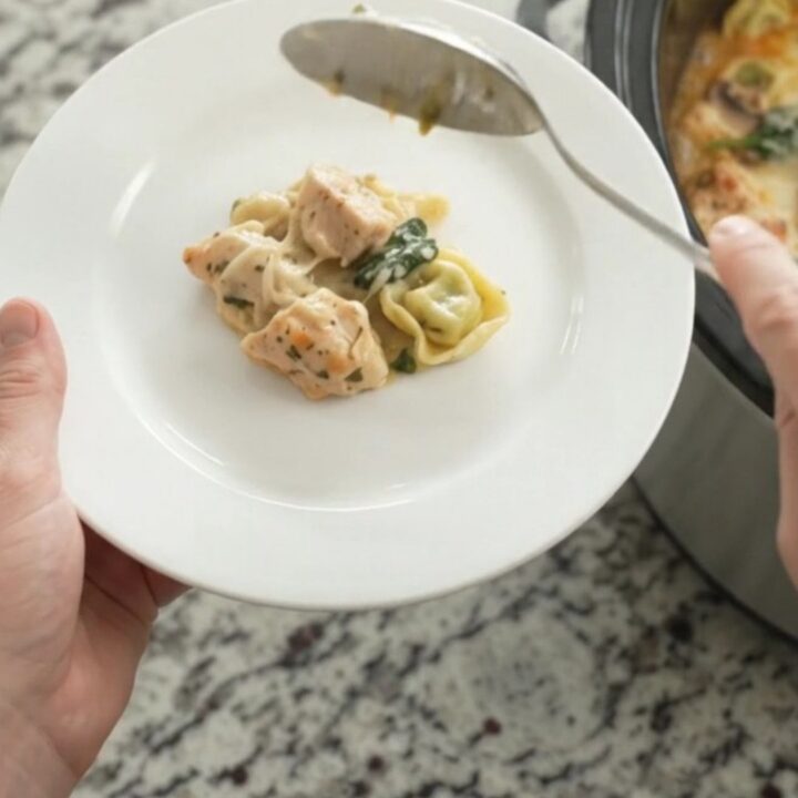Creamy crockpot chicken spinach tortellini in a black slow cooker, topped with melted Italian cheeses