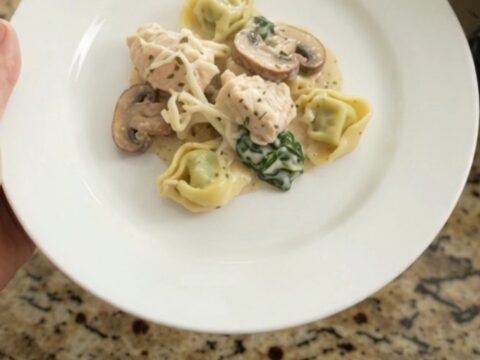 Slow cooker with creamy chicken and tortellini, topped with melted cheese and herbs.