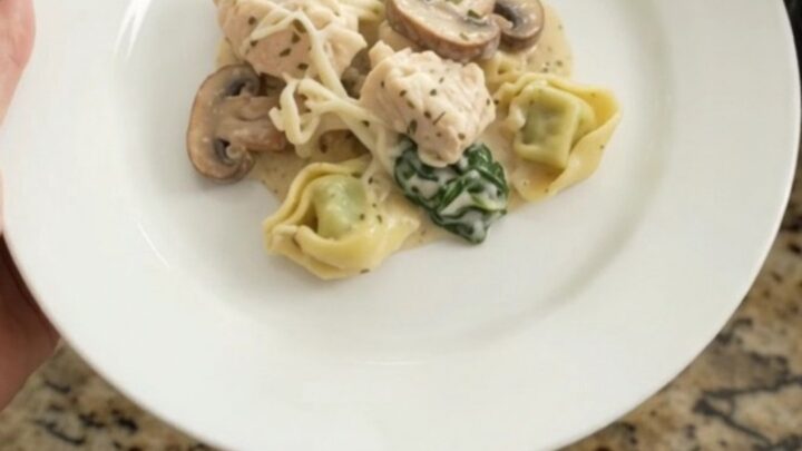 Slow cooker with creamy chicken and tortellini, topped with melted cheese and herbs.