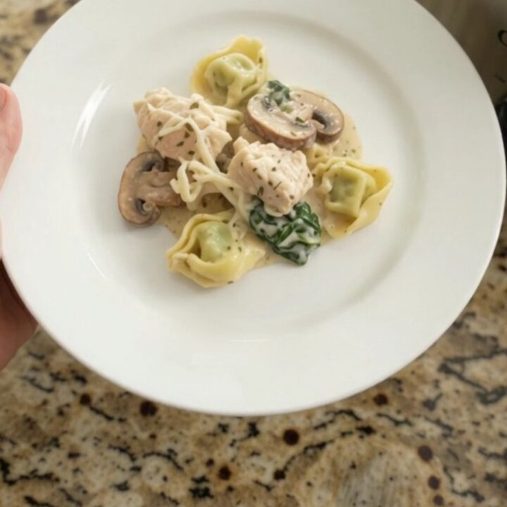 Slow cooker with creamy chicken and tortellini, topped with melted cheese and herbs.