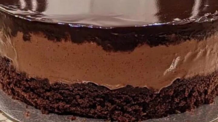 A pristine chocolate mousse cake with a glossy mirror glaze on a silver board.