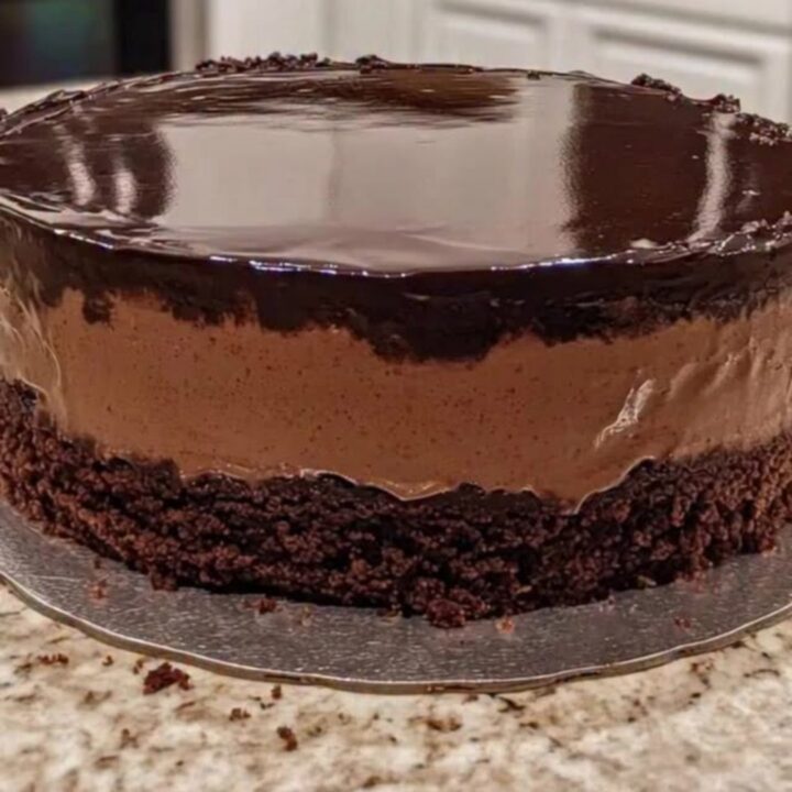 A pristine chocolate mousse cake with a glossy mirror glaze on a silver board.