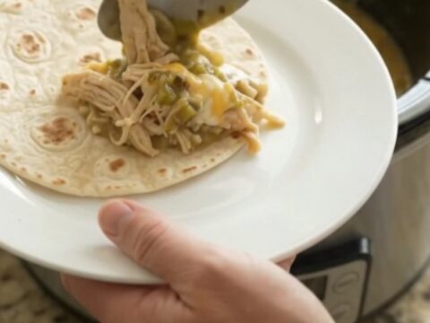 Creamy salsa verde chicken in a slow cooker, topped with melted cheese and green chiles.