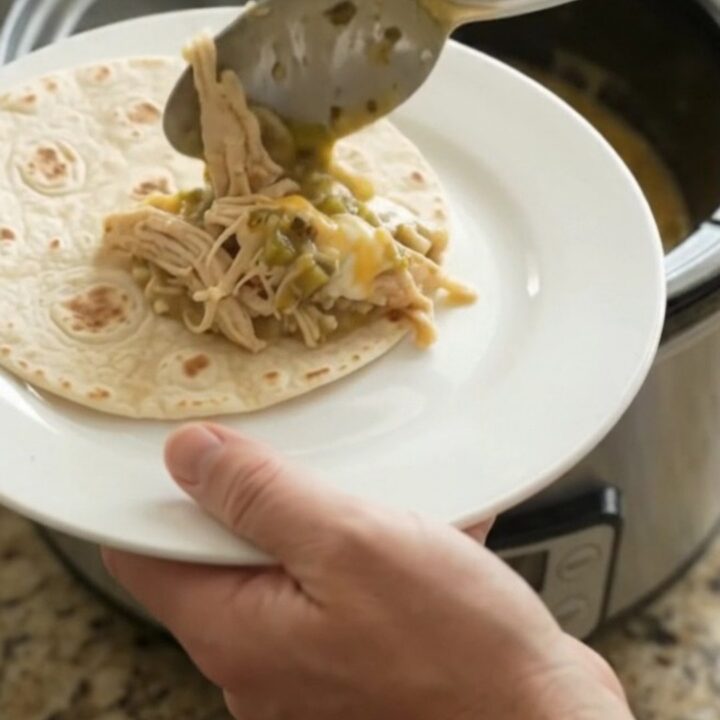 Creamy salsa verde chicken in a slow cooker, topped with melted cheese and green chiles.