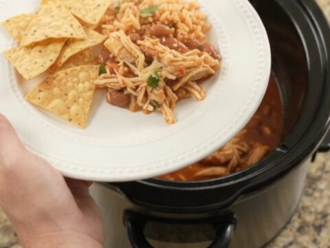Slow cooker filled with shredded chicken in red enchilada sauce, topped with melted cheese and beans.