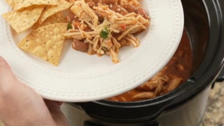 Slow cooker filled with shredded chicken in red enchilada sauce, topped with melted cheese and beans.