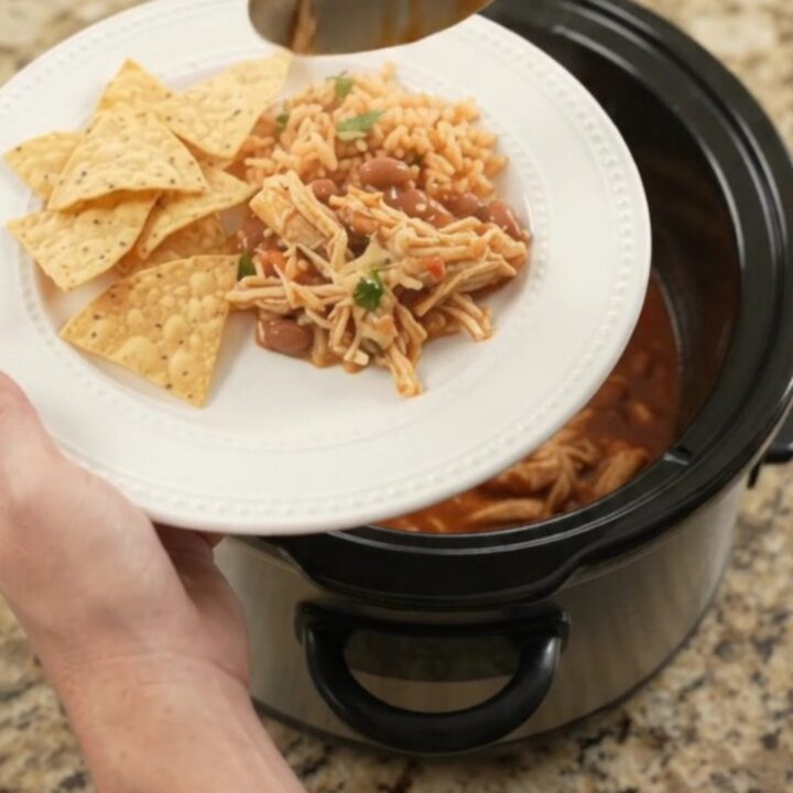 Slow cooker filled with shredded chicken in red enchilada sauce, topped with melted cheese and beans.