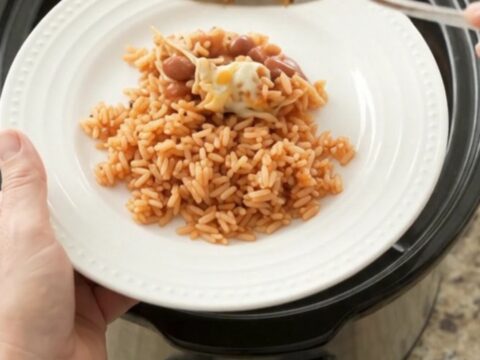 Slow cooker filled with shredded chicken in red enchilada sauce, topped with melted Oaxaca cheese and pinto beans