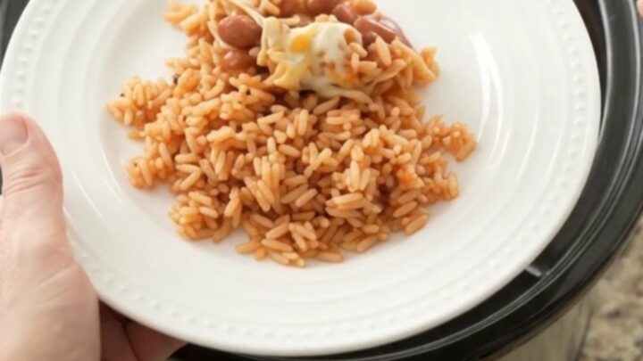 Slow cooker filled with shredded chicken in red enchilada sauce, topped with melted Oaxaca cheese and pinto beans