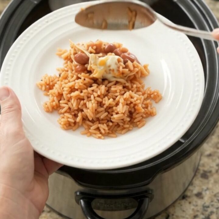 Slow cooker filled with shredded chicken in red enchilada sauce, topped with melted Oaxaca cheese and pinto beans