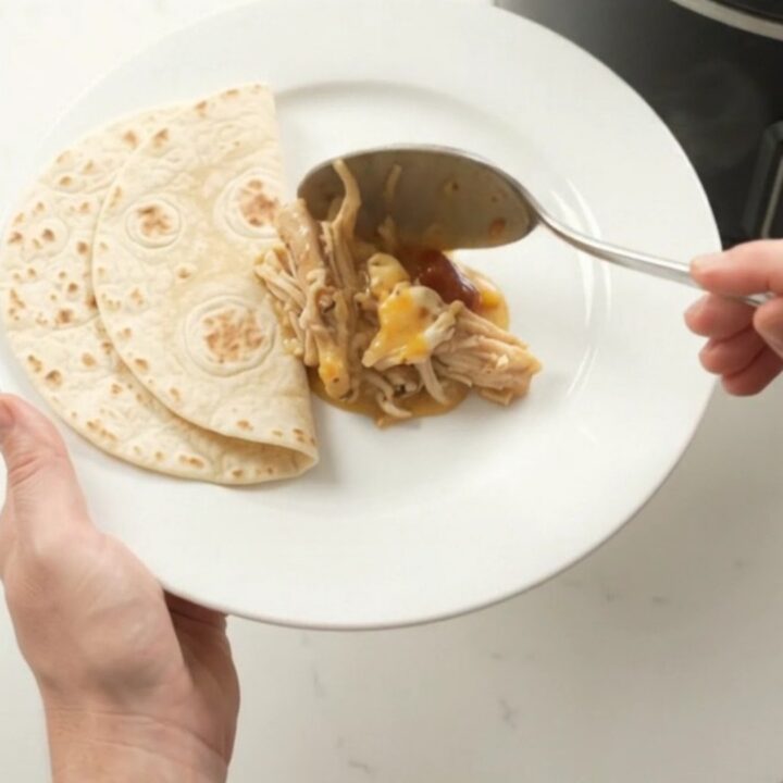 Slow cooker with creamy chipotle pineapple chicken, topped with melted cheese and steam rising