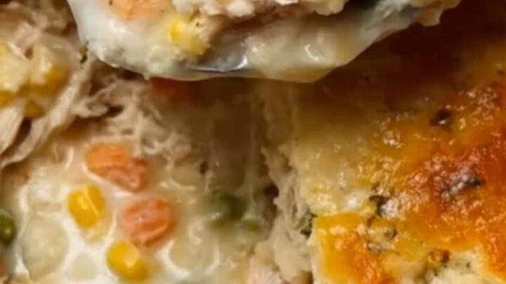A golden-brown Cheddar Bay chicken cobbler in a white ceramic baking dish with a spoon lifting a portion.