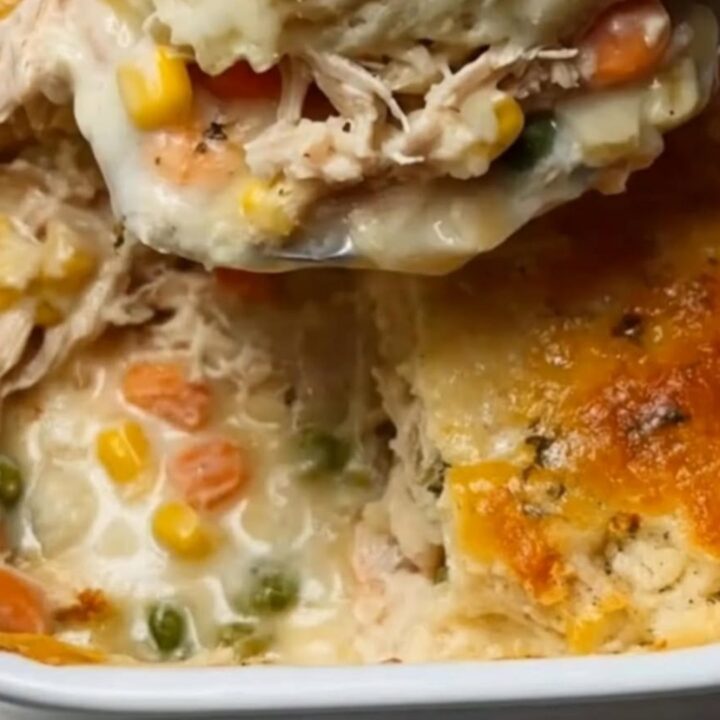 A golden-brown Cheddar Bay chicken cobbler in a white ceramic baking dish with a spoon lifting a portion.