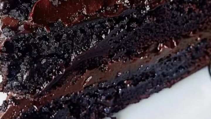 A towering triple-layer chocolate fudge cake on a white plate with glossy ganache.