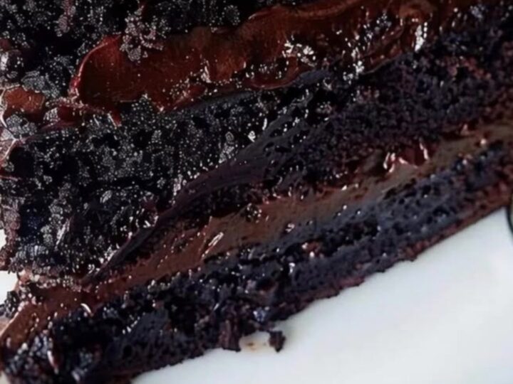 A towering triple-layer chocolate fudge cake on a white plate with glossy ganache.