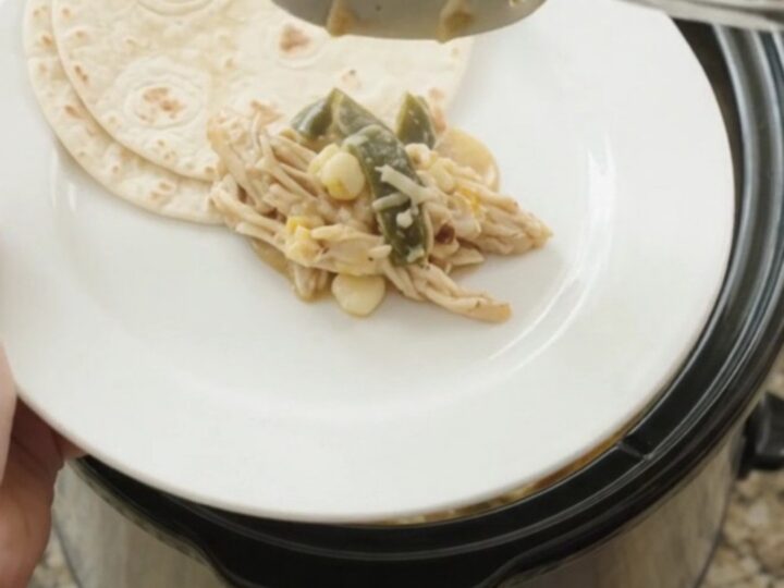 Creamy slow-cooker fiesta chicken with shredded chicken, hominy, and melted Monterey Jack in a black crockpot.