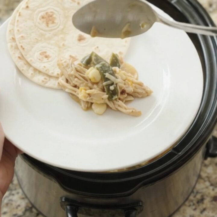 Creamy slow-cooker fiesta chicken with shredded chicken, hominy, and melted Monterey Jack in a black crockpot.