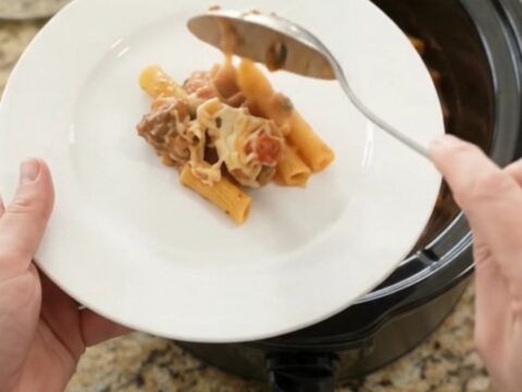 Slow cooker filled with bubbling cheesy chicken baked ziti, golden top with herbs