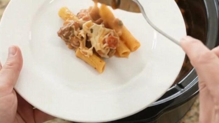 Slow cooker filled with bubbling cheesy chicken baked ziti, golden top with herbs