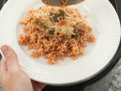 Slow cooker filled with shredded chicken, melted cheese, poblano peppers, and hominy, with a spoon lifting a cheesy scoop.