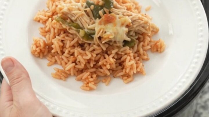 Slow cooker filled with shredded chicken, melted cheese, poblano peppers, and hominy, with a spoon lifting a cheesy scoop.