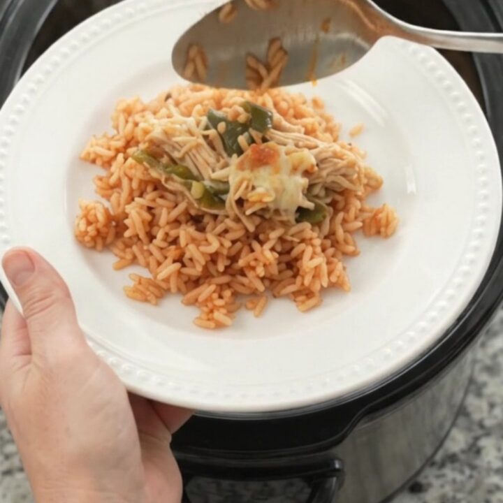 Slow cooker filled with shredded chicken, melted cheese, poblano peppers, and hominy, with a spoon lifting a cheesy scoop.
