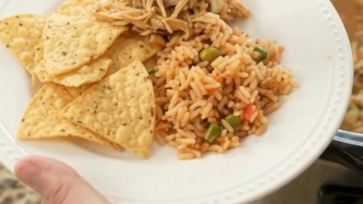 A slow cooker filled with shredded chicken, beans, and melted pepper jack cheese, with a spoon lifting a cheesy scoop.