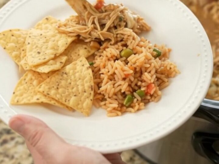 A slow cooker filled with shredded chicken, beans, and melted pepper jack cheese, with a spoon lifting a cheesy scoop.