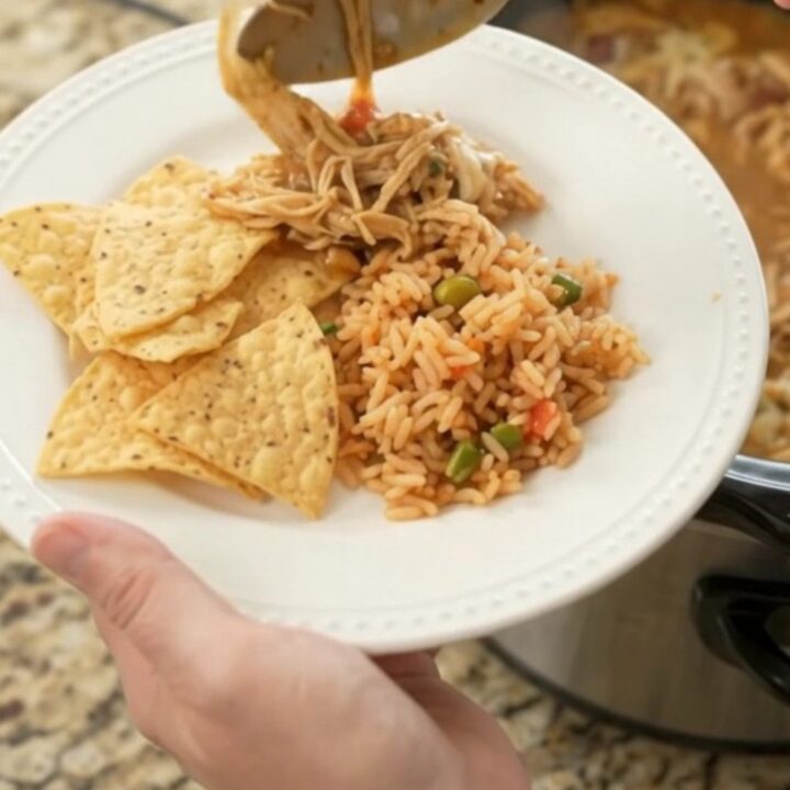A slow cooker filled with shredded chicken, beans, and melted pepper jack cheese, with a spoon lifting a cheesy scoop.