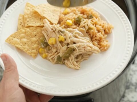 Slow cooker fiesta chicken with creamy queso sauce, green chiles, and corn in a black crockpot