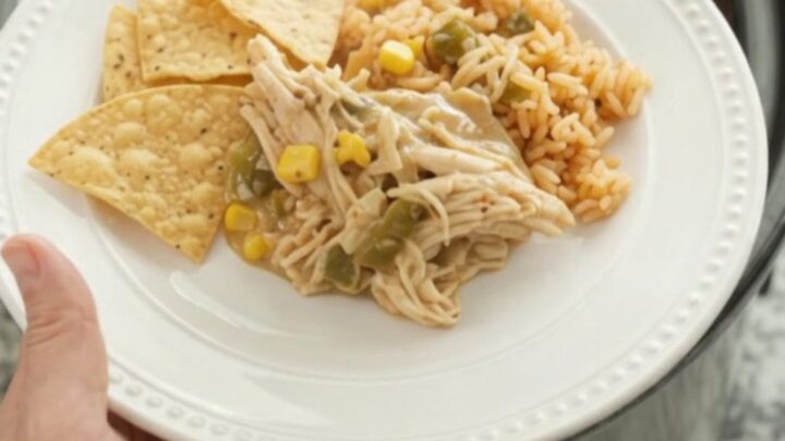 Slow cooker fiesta chicken with creamy queso sauce, green chiles, and corn in a black crockpot