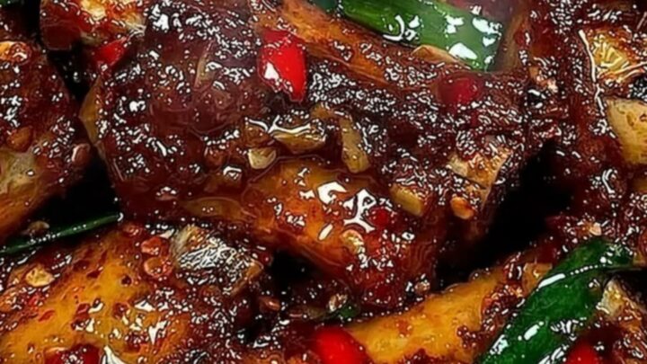 Extreme close-up of a tender, glistening rib being pulled apart with tongs, showing steam and sticky sauce.