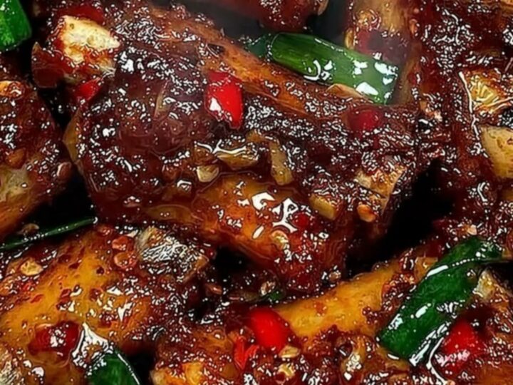 Extreme close-up of a tender, glistening rib being pulled apart with tongs, showing steam and sticky sauce.