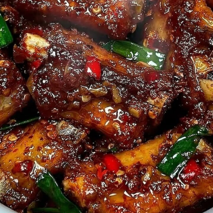 Extreme close-up of a tender, glistening rib being pulled apart with tongs, showing steam and sticky sauce.
