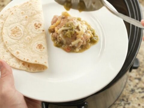Creamy salsa verde chicken thighs in a black Crockpot, topped with melted Monterey Jack and sour cream sauce.