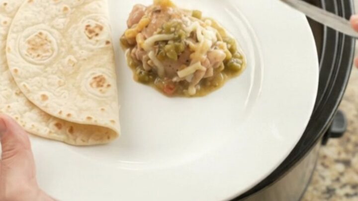 Creamy salsa verde chicken thighs in a black Crockpot, topped with melted Monterey Jack and sour cream sauce.
