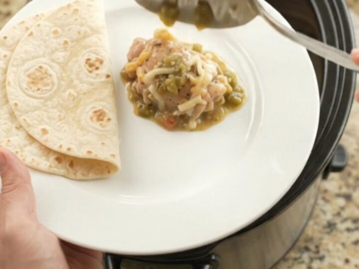 Creamy salsa verde chicken thighs in a black Crockpot, topped with melted Monterey Jack and sour cream sauce.