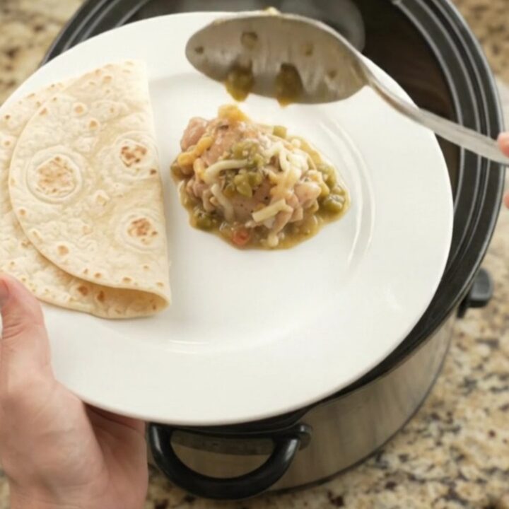 Creamy salsa verde chicken thighs in a black Crockpot, topped with melted Monterey Jack and sour cream sauce.