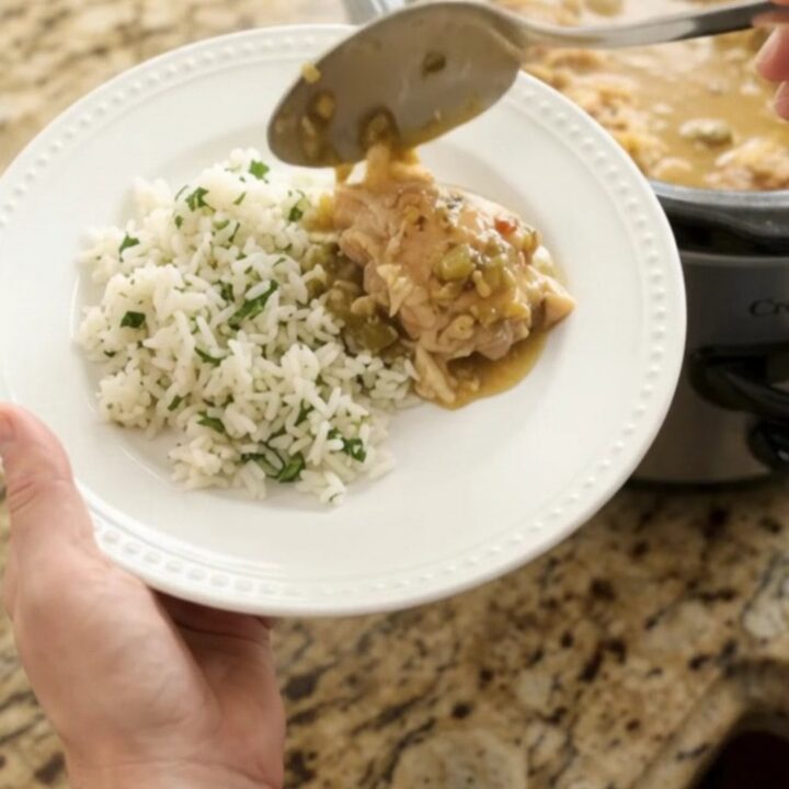 Creamy cheddar salsa verde chicken thighs in a slow cooker with melted cheese and green sauce.