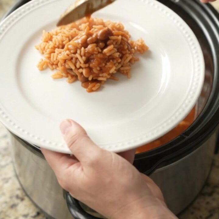 Slow cooker filled with chicken thighs in red enchilada sauce topped with melted Oaxaca cheese and beans