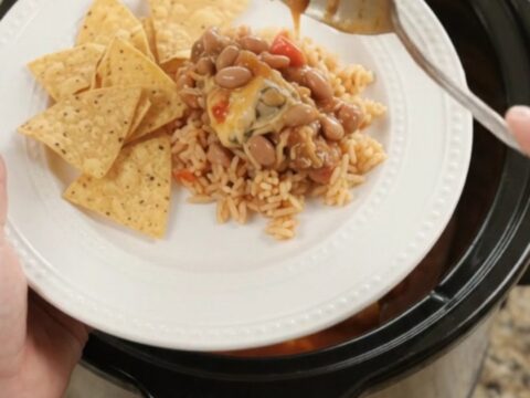Slow cooker filled with chicken thighs in red enchilada sauce, topped with melted pepper jack and queso blanco