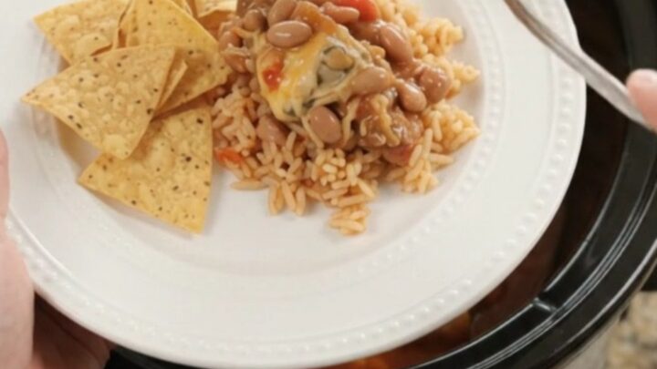 Slow cooker filled with chicken thighs in red enchilada sauce, topped with melted pepper jack and queso blanco
